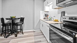 A compact kitchen with a dining area, featuring a microwave, oven, and a small table with chairs. - 30-Night Minimum Studio Near Main Street (St Charles)