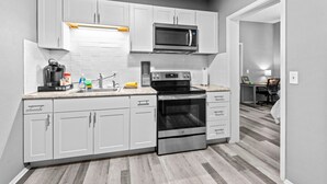 A modern kitchen with white cabinets, a microwave, an oven, and a sink. - 30-Night Minimum Studio Near Main Street (St Charles)