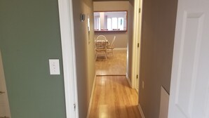 Un pasillo con suelo de madera, una puerta blanca a la derecha y una silla al fondo.