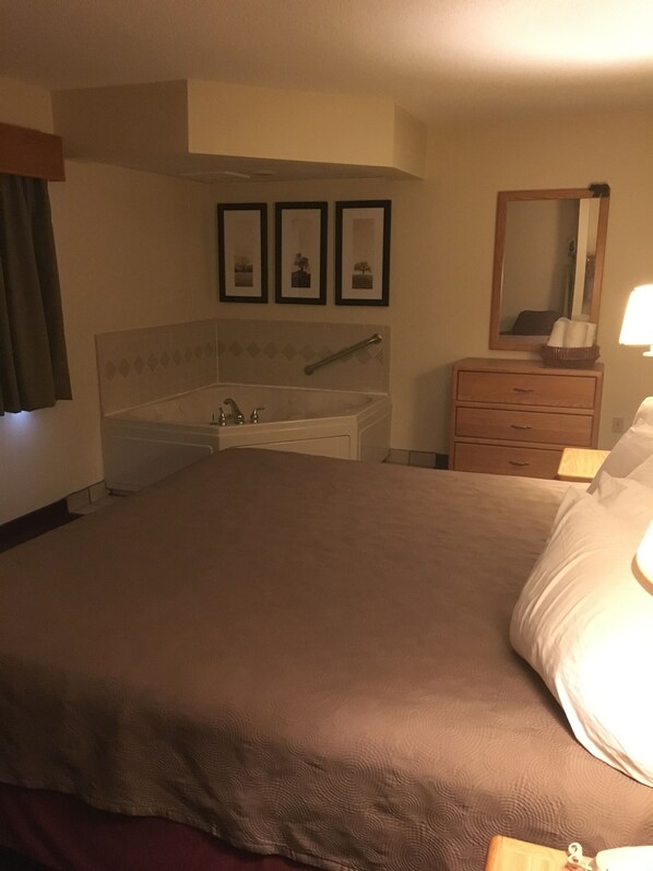 Une chambre d’hôtel avec un grand lit, une table de chevet avec une lampe, une commode, un miroir et un tableau encadré au mur.