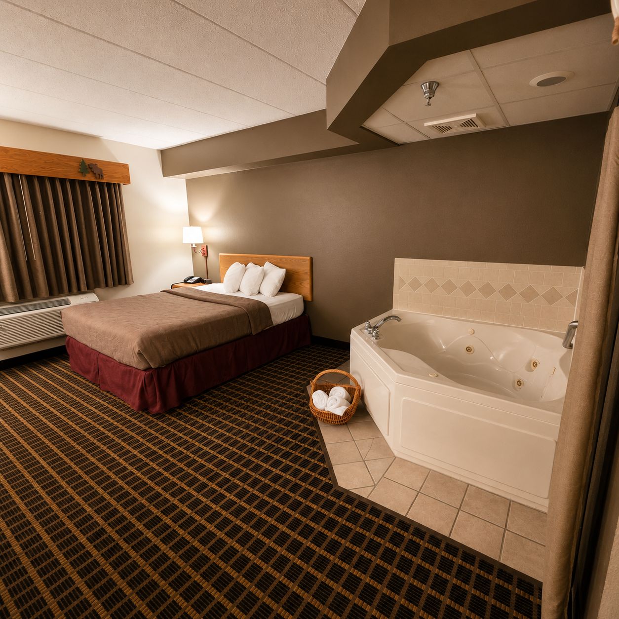 A hotel room with a bed, a bedside table with a lamp, a bathroom with a bathtub, and a patterned carpet.
