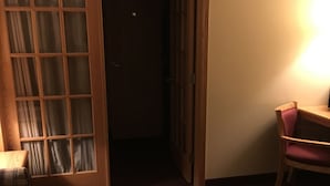 Una habitación con un banco de madera, un sofá a cuadros, una puerta de madera con paneles de vidrio y un sillón con cojín.