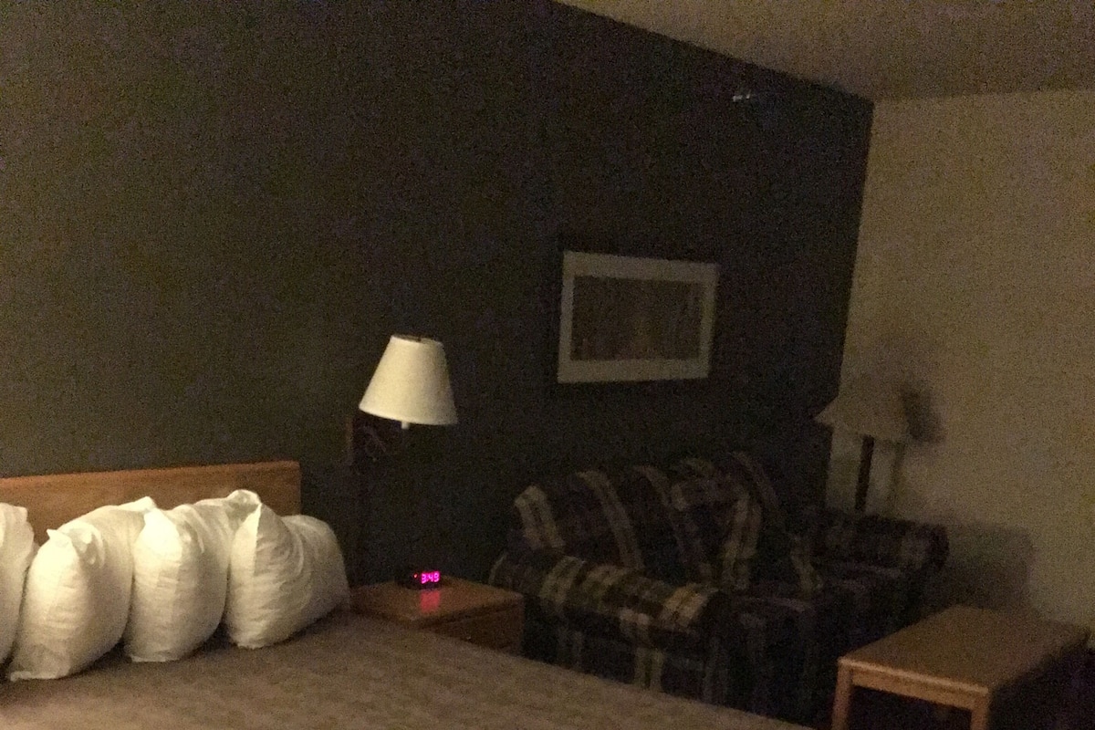 Ein Hotelzimmer mit einem großen Bett, einem Nachttisch, einer Lampe und einem Sofa.