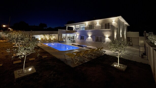 A modern two-story house with a swimming pool, outdoor seating, and well-lit exterior.