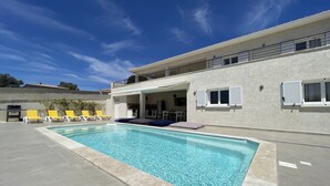 A swimming pool with lounge chairs, a covered patio, and a two-story building with a balcony.