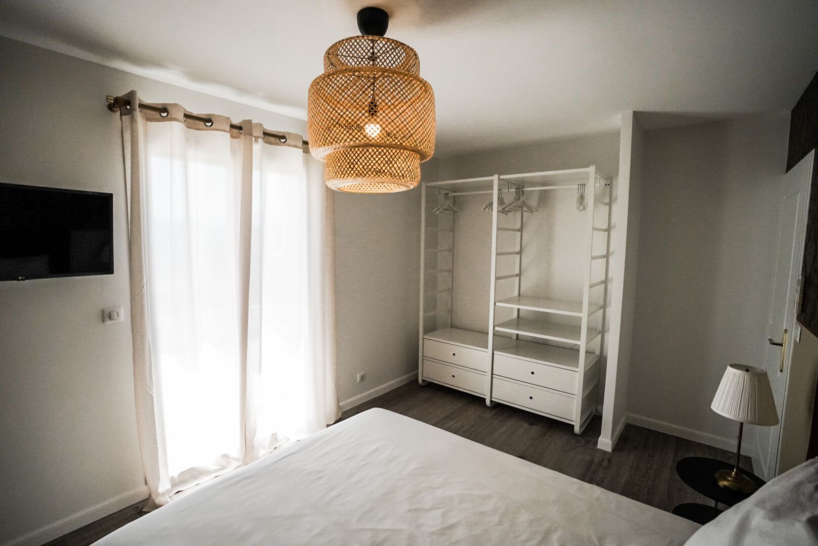 A bedroom with a bed, a wardrobe, a hanging light fixture, and a bedside table.