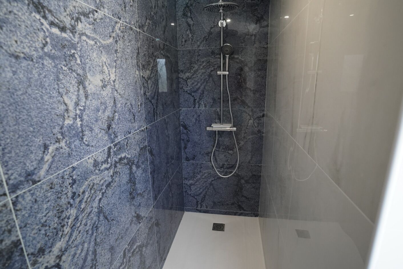 A modern bathroom with a glass-enclosed shower, marble walls, and a visible control panel.