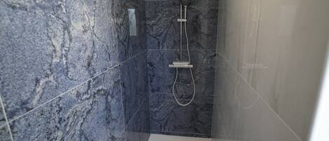A modern bathroom with a glass-enclosed shower, marble walls, and a visible control panel.