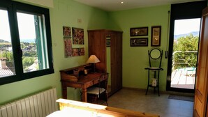 Un dormitorio con cama, escritorio, silla, armario de madera y vistas al exterior.