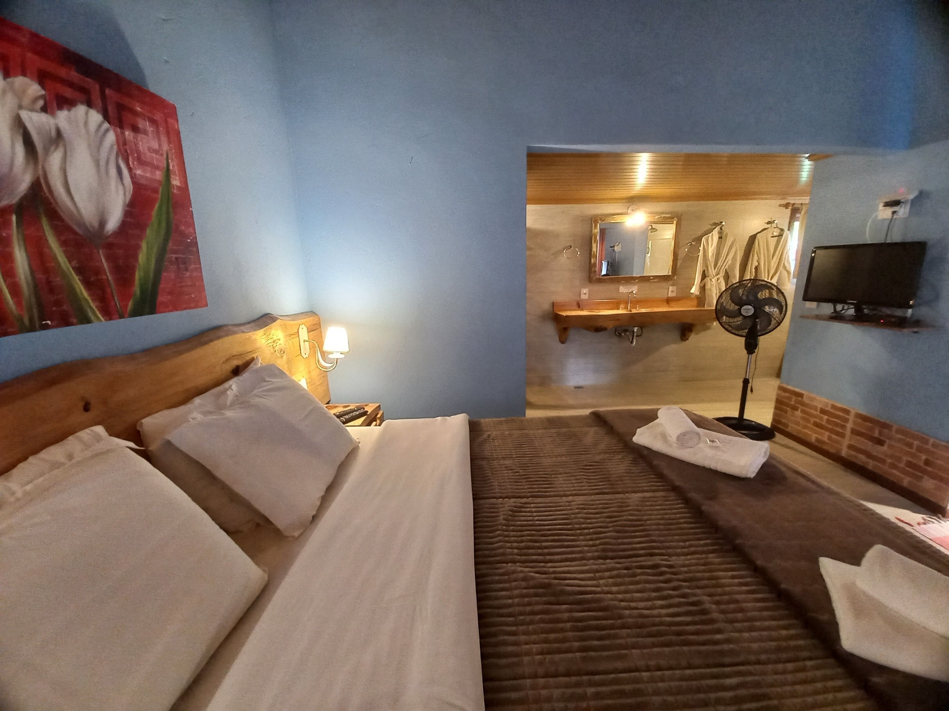 A hotel room with a bed, a nightstand with a lamp, a wall-mounted TV, and a bathroom visible through an open door.