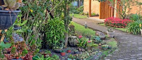 A garden with various potted plants and a brick pathway leading to a building with a tiled roof.