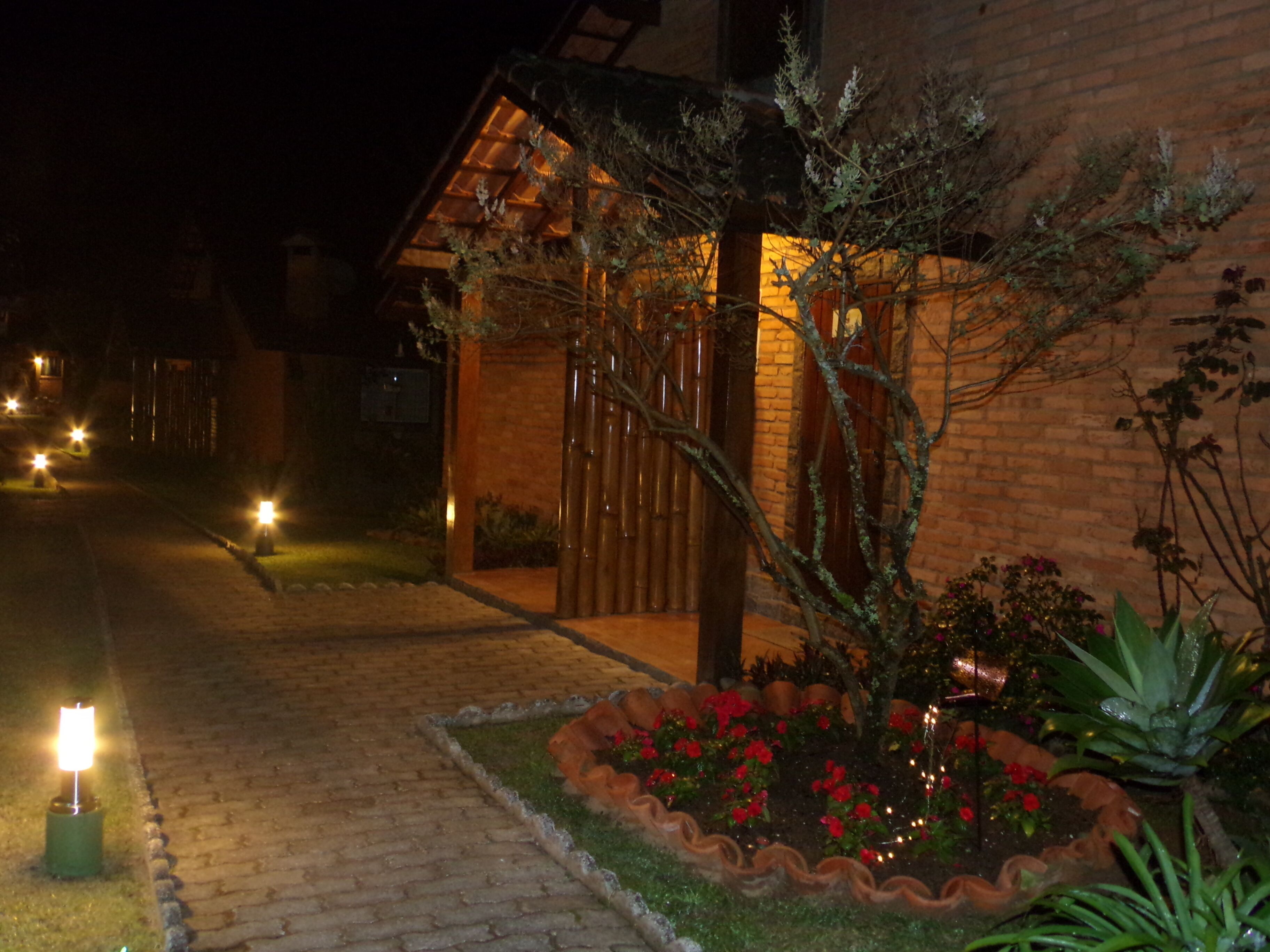 A brick building with a wooden porch and a garden with red flowers.