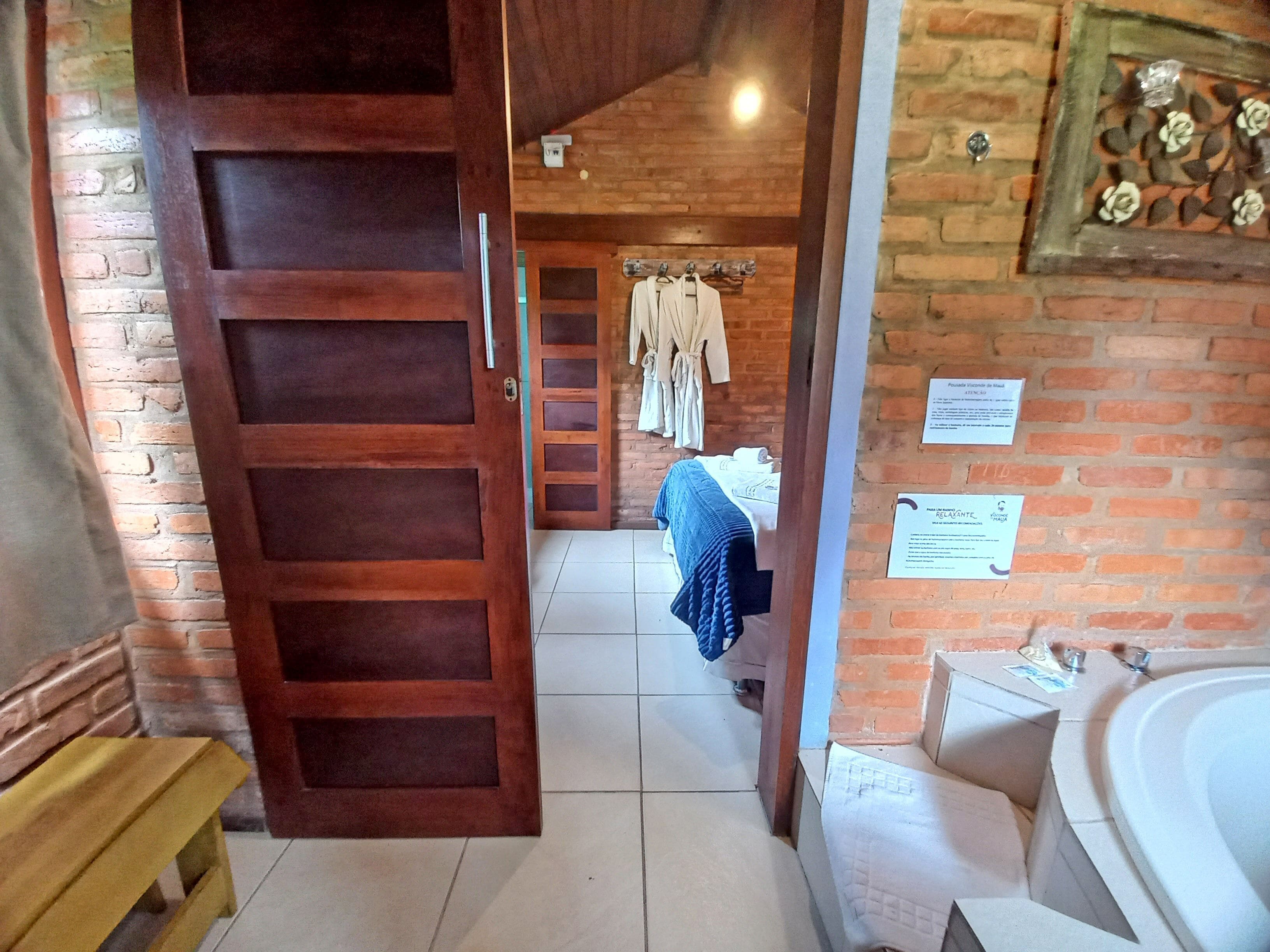 Una porta de fusta que dona a una habitació amb un llit, una barra de tovalloles i una paret de maó.