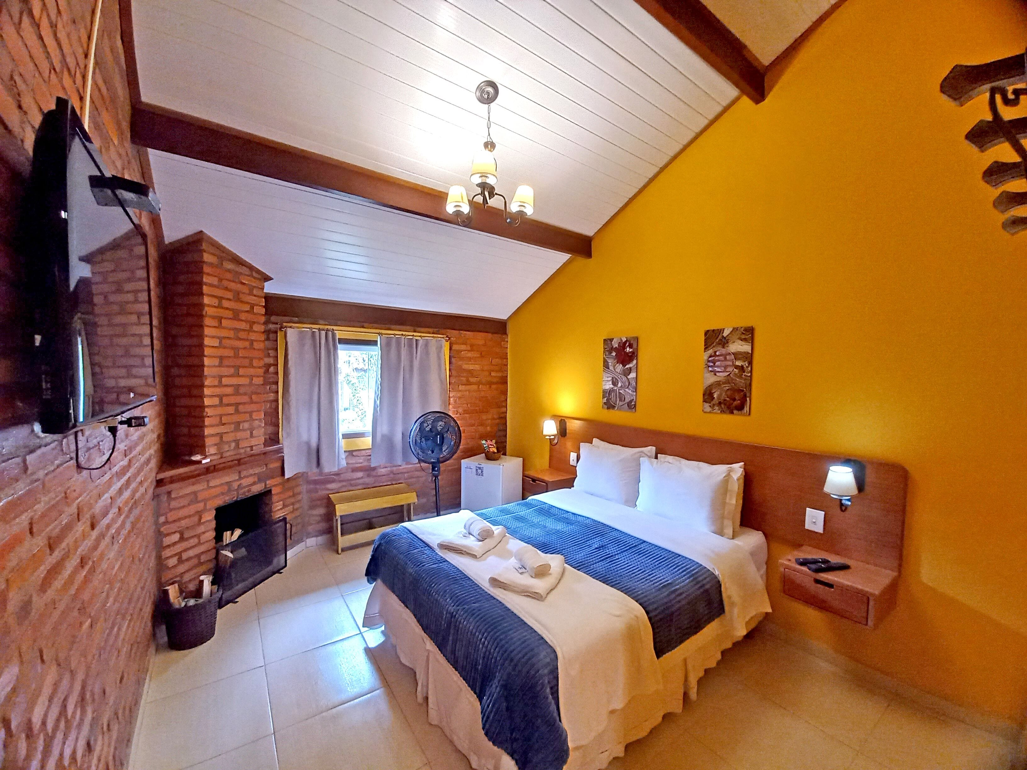 Habitación de hotel con chimenea de ladrillo, cama con ropa de cama blanca, ventilador de techo y obras de arte en las paredes.