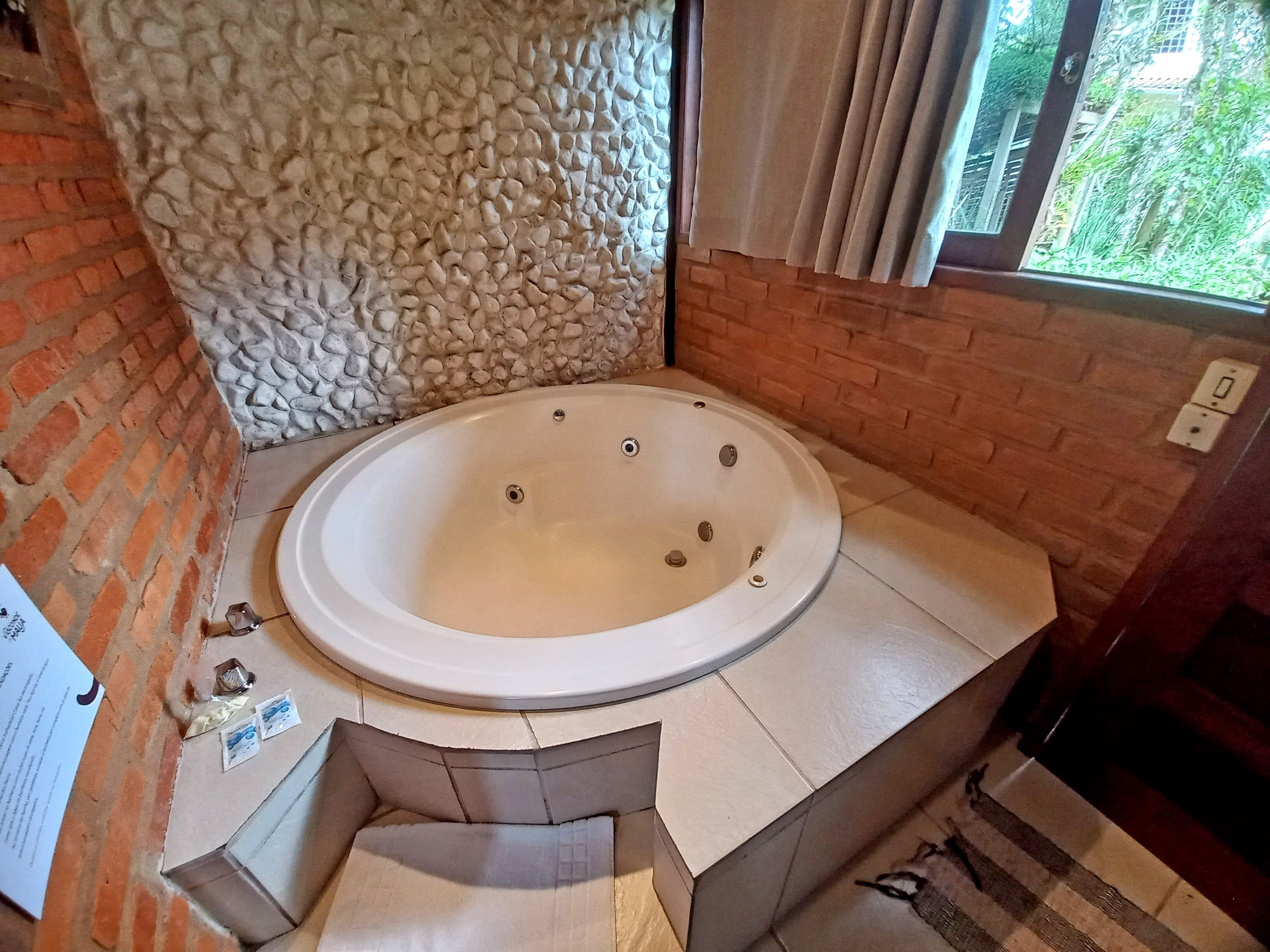 A bathroom with a stone wall, a brick wall, a bathtub, and a window with curtains.