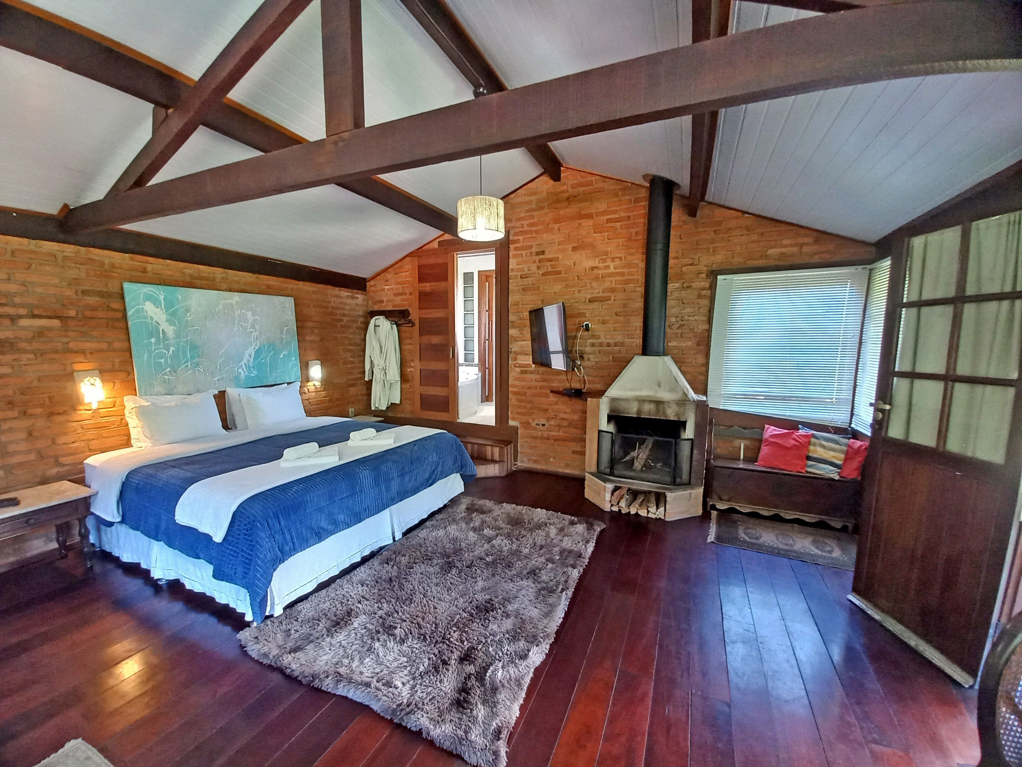 A bedroom with a large bed, a fireplace, wooden beams, and a view of the outside.