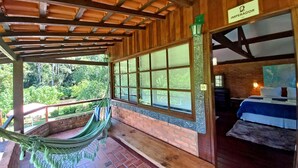 A wooden room with a bed, a hammock, and a view of greenery outside. - Pousada Visconde de Mauá (Resende)