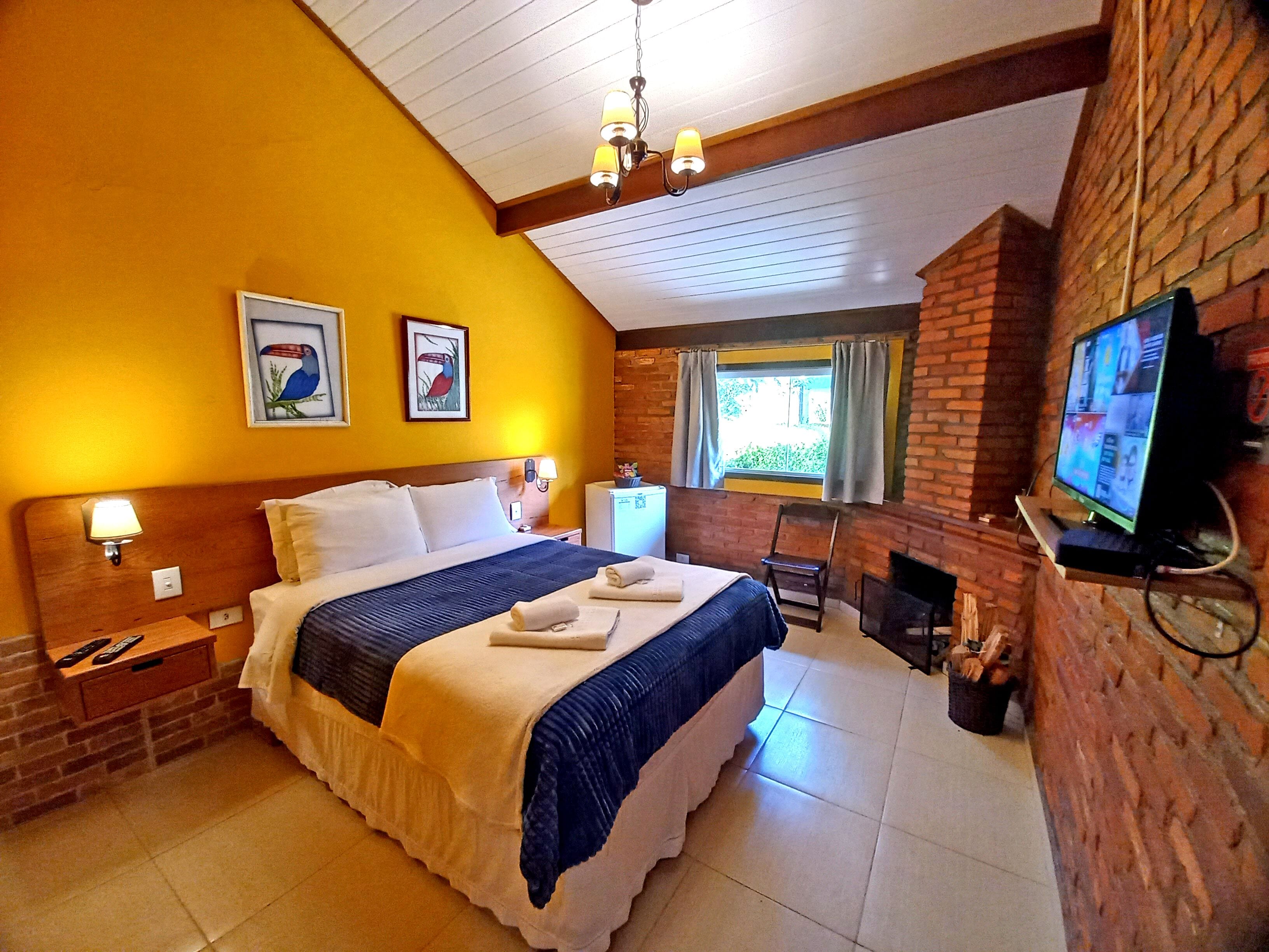 A hotel room with a large bed, a television, a fireplace, and artwork on the walls.