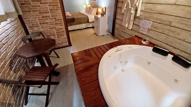 A room with a wooden floor, a wooden bench, a white bathtub, and a bed with a white headboard. - Pousada Visconde de Mauá (Resende)
