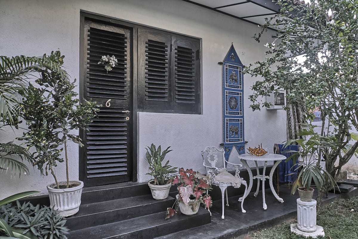A white building with black shutters, a blue door, and a white chair outside.