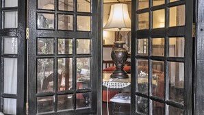 A room with a large window with a black frame, a table lamp, and a lace tablecloth. - The Icebear Guesthouse (Negombo)