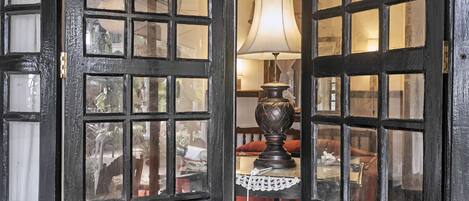 A room with a large window with a black frame, a table lamp, and a lace tablecloth.