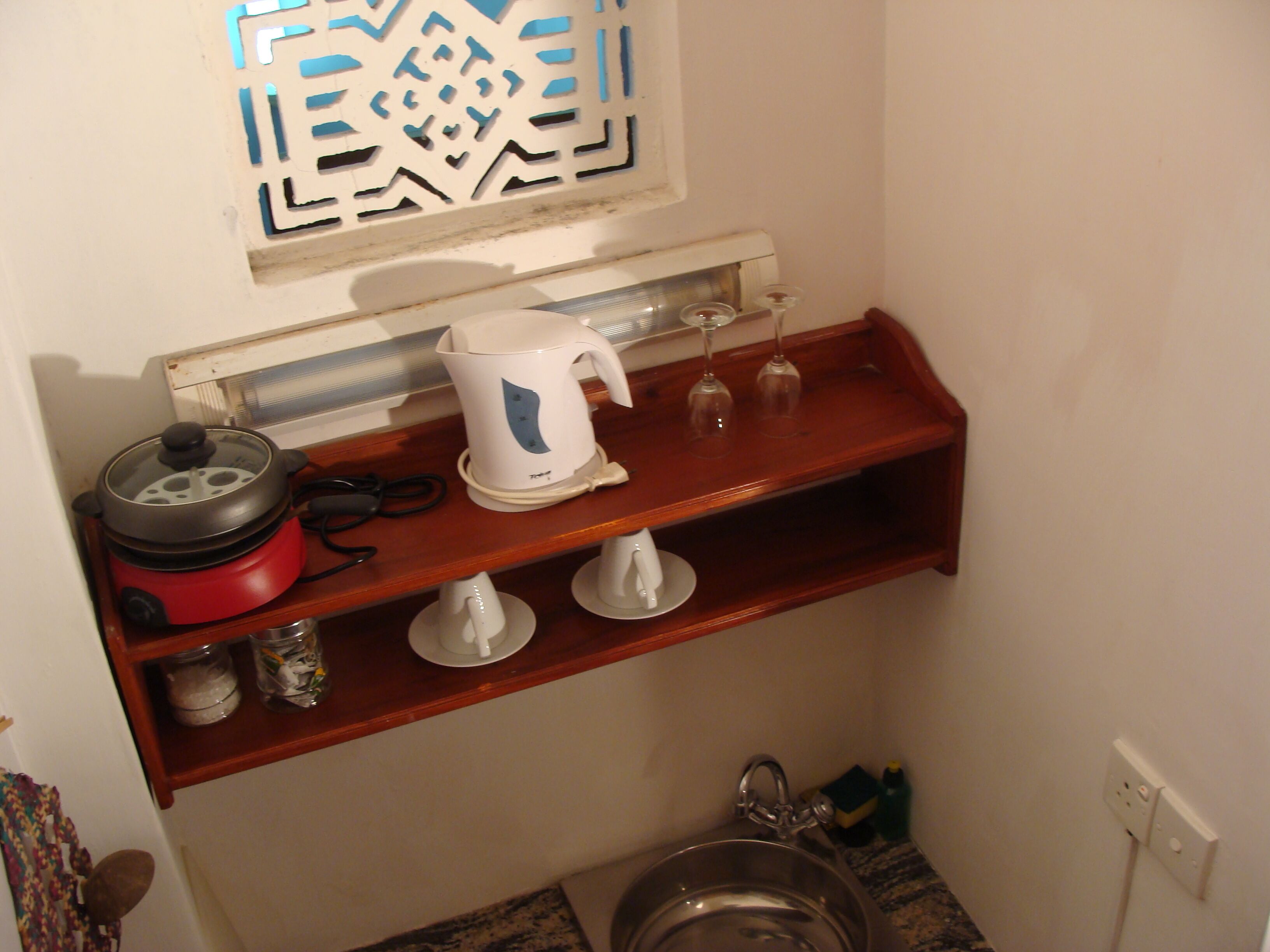 A kitchen with a wooden shelf holding a kettle, a red appliance, and a glass container.