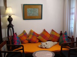 Quarto com cama, almofadas coloridas, luminária, obra de arte emoldurada e uma cadeira.
