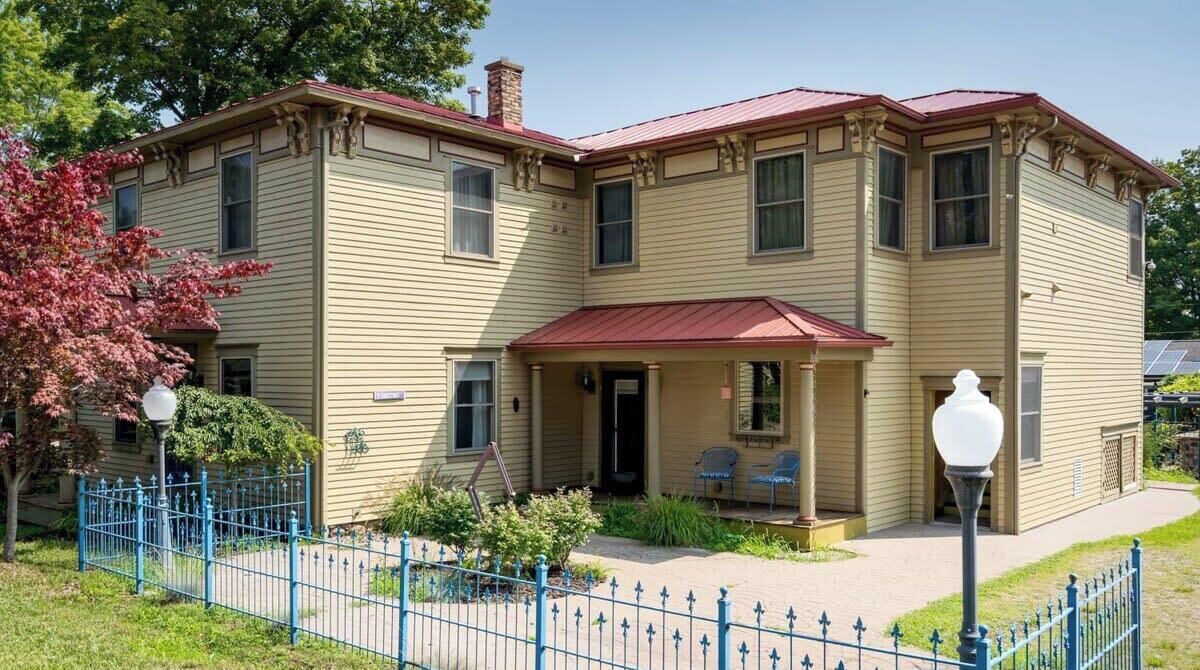 Un bâtiment à deux étages avec un toit rouge, une véranda avec des chaises et une clôture bleue.