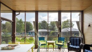 A covered outdoor area with large windows, wicker furniture, and a table with a box. - Lake Life Getaway - Condo near downtown! (Douglas)