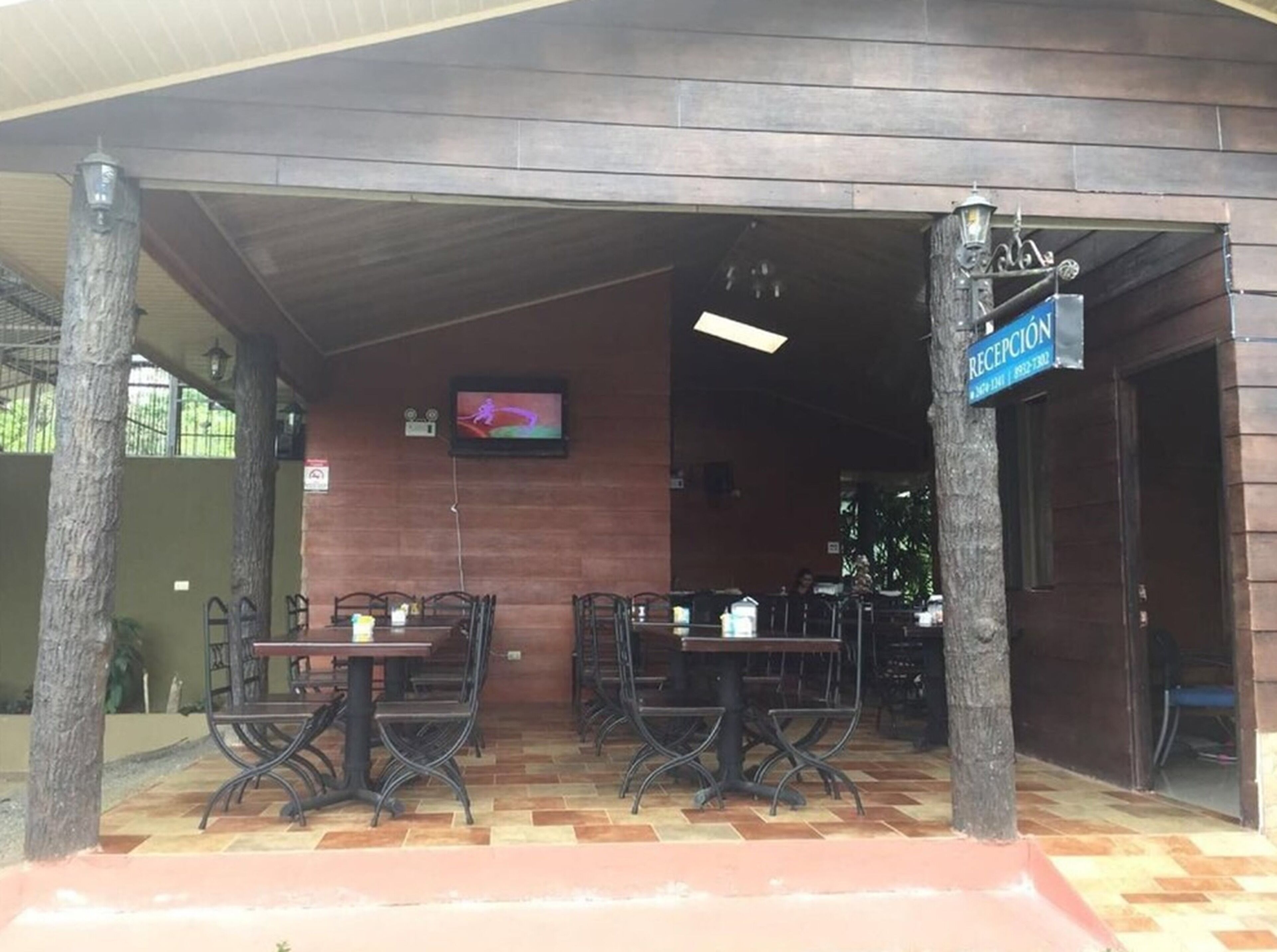 An outdoor cafe area with tables and chairs, a television mounted on the wall, and a reception sign.
