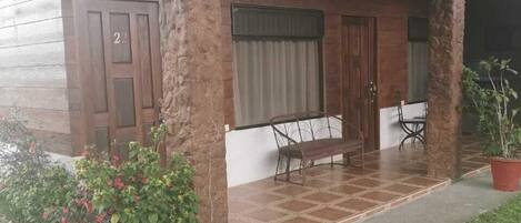 A covered porch with a bench and two chairs, a wooden door with the number 22, and a potted plant.