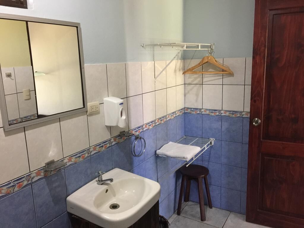 Un baño con lavamanos, espejo, toallero y una puerta de madera.
