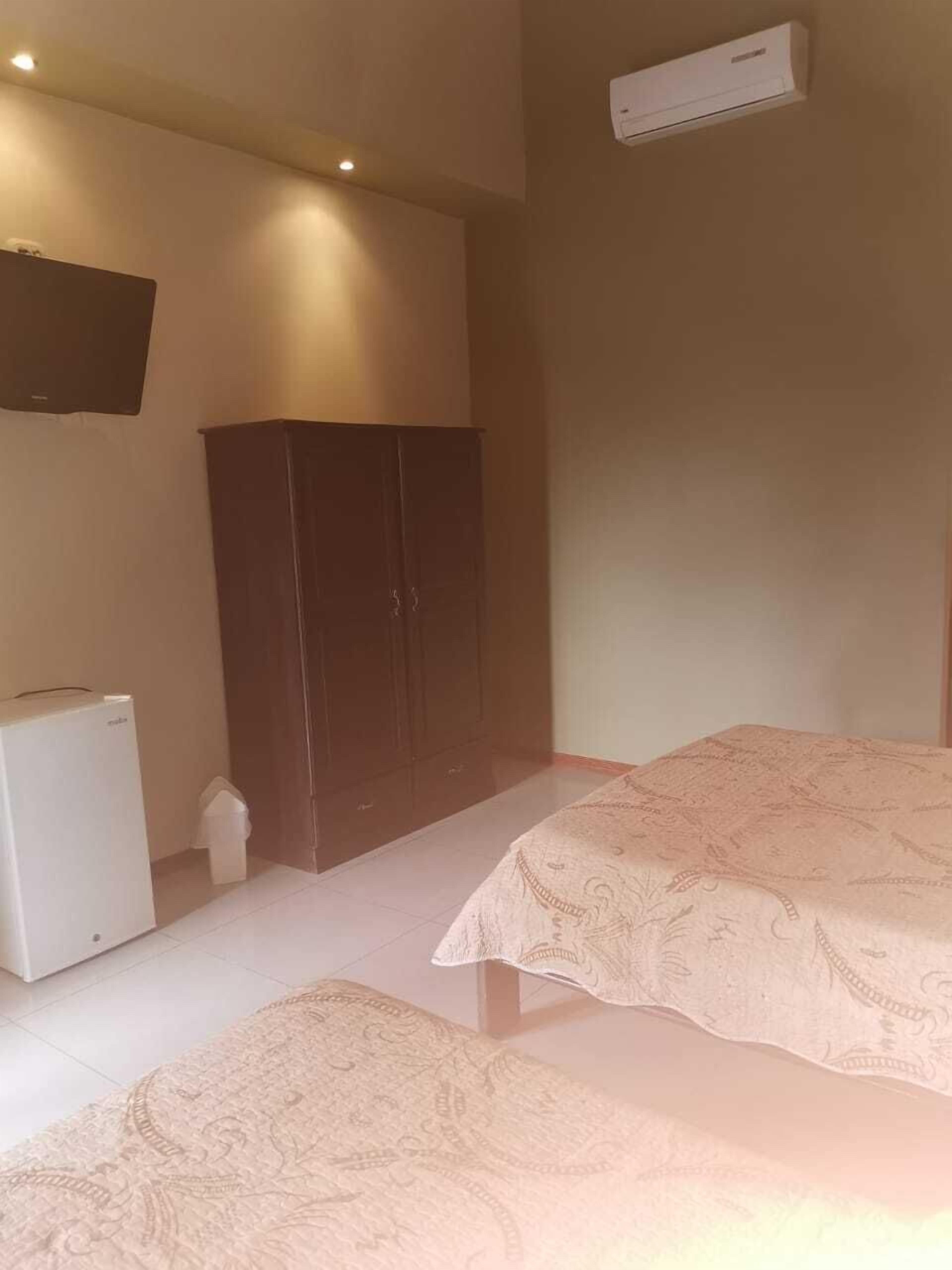 Quarto com duas camas, um guarda-roupa, um pequeno eletrodoméstico branco e uma televisão montada.