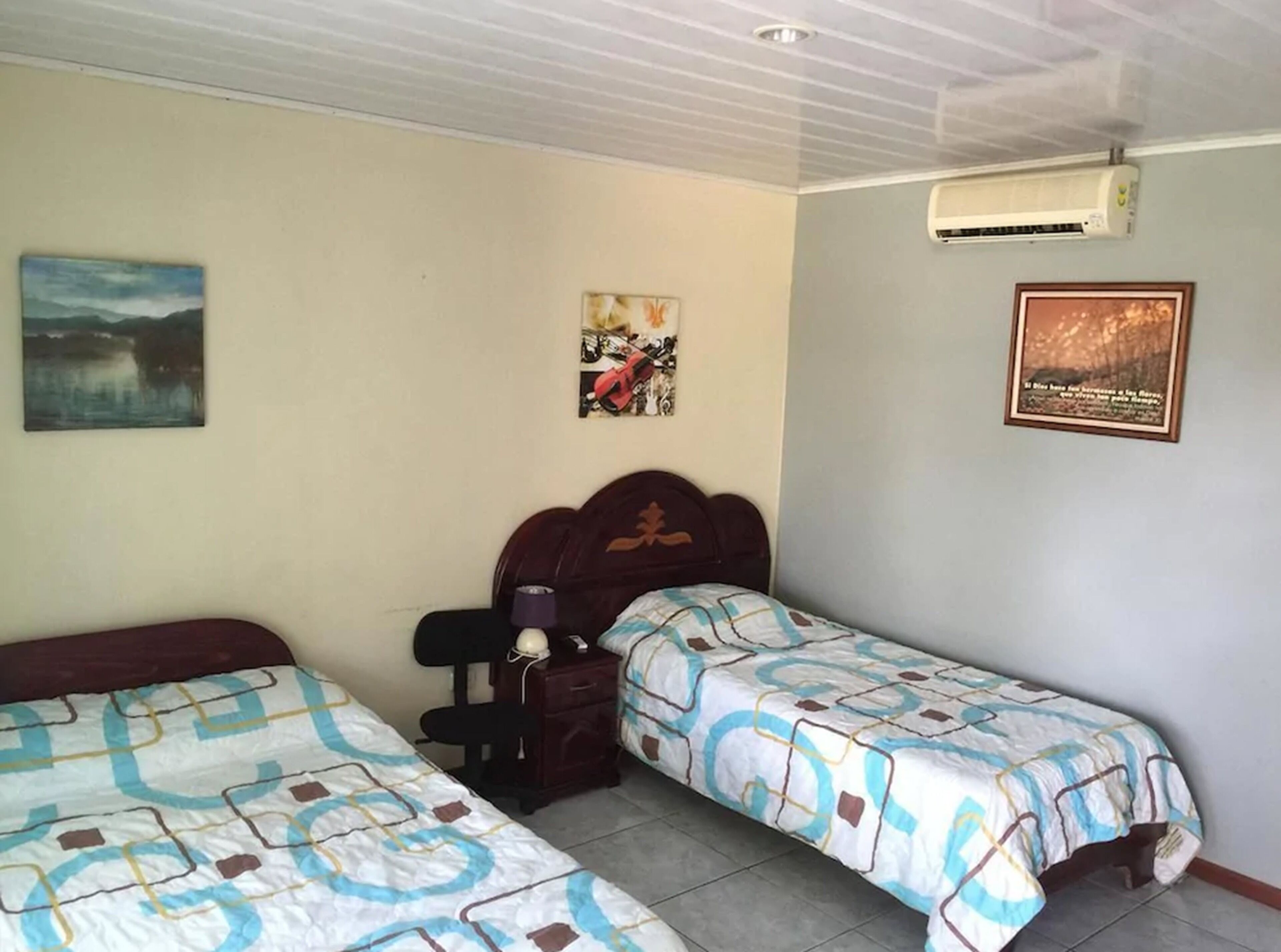 A bedroom with two single beds, a nightstand, a lamp, and wall art.