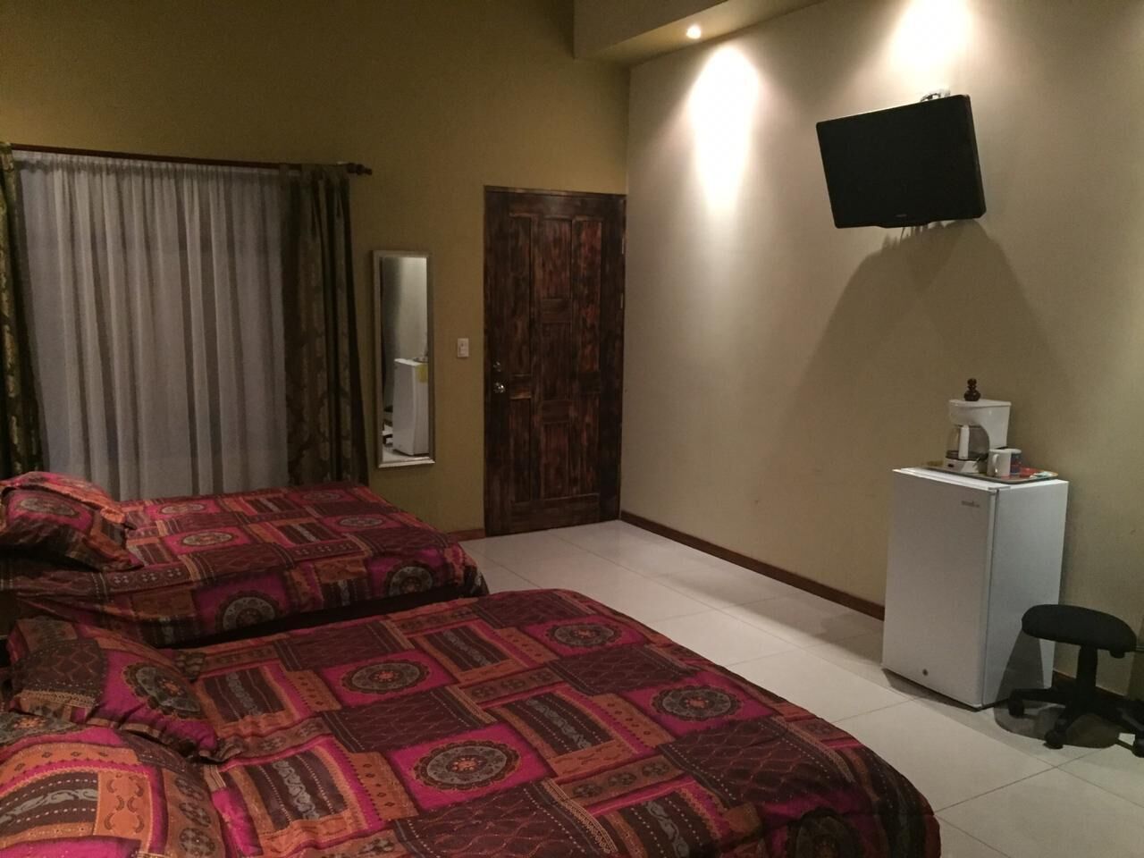 A bedroom with two beds, a television, a small refrigerator, and a desk with a chair.