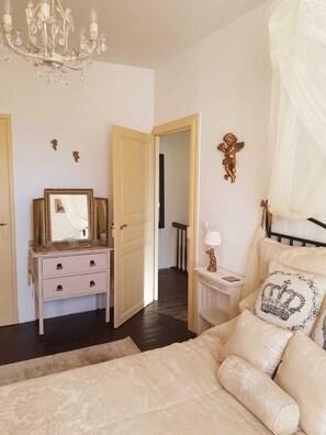 Ein Schlafzimmer mit einem Bett, einem Schminktisch, einem Spiegel, einer Chandelier und einer Tür zu einem anderen Raum.