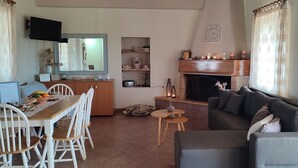 Ein Wohnzimmer mit Kamin, einer Couch, einem Esstisch mit Stühlen und einem an der Wand befestigten Fernseher.