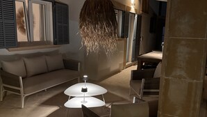 A cozy living area with a sofa, a wicker chair, and a round table with a lamp. - Casa Sigrunella++with infinity pool (12x4m)++ in Cala Llombards (Cala Llombards)