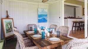 Comedor con mesa de madera dispuesta para seis personas, sillas de mimbre y un ventilador de techo.