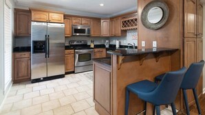 A kitchen with wooden cabinets, stainless steel appliances, a bar counter, and two blue bar stools.