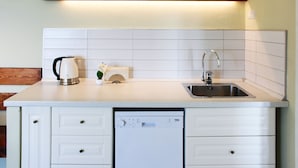 Een keuken met witte kasten, een vaatwasser, een spoelbak en een houten plank boven het aanrecht.