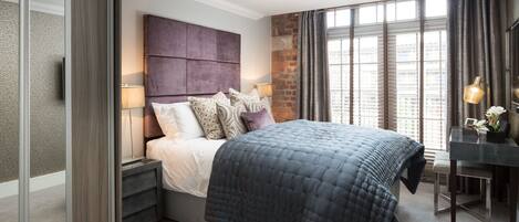 A modern bedroom with a large bed, a nightstand, a desk, and a brick accent wall.