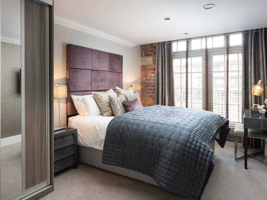 Une chambre moderne avec un grand lit, une table de chevet, un bureau et un mur décoratif en briques.