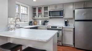 A modern kitchen with white cabinets, a stainless steel refrigerator, a microwave, and a large island with two stools. - Oxford Square! Amazing Location! (Oxford)