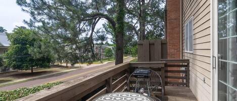 A wooden deck with a round table and chairs, a brick wall, and a view of a street and trees.