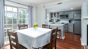 A dining area with a table set for four, a kitchen with modern appliances, and a view through large windows. - Oxford Square! Amazing Location! (Oxford)
