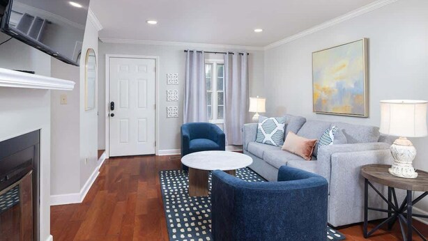 A living room with a fireplace, a television, a sofa, a coffee table, and a painting on the wall. - Oxford Square! Amazing Location! (Oxford)