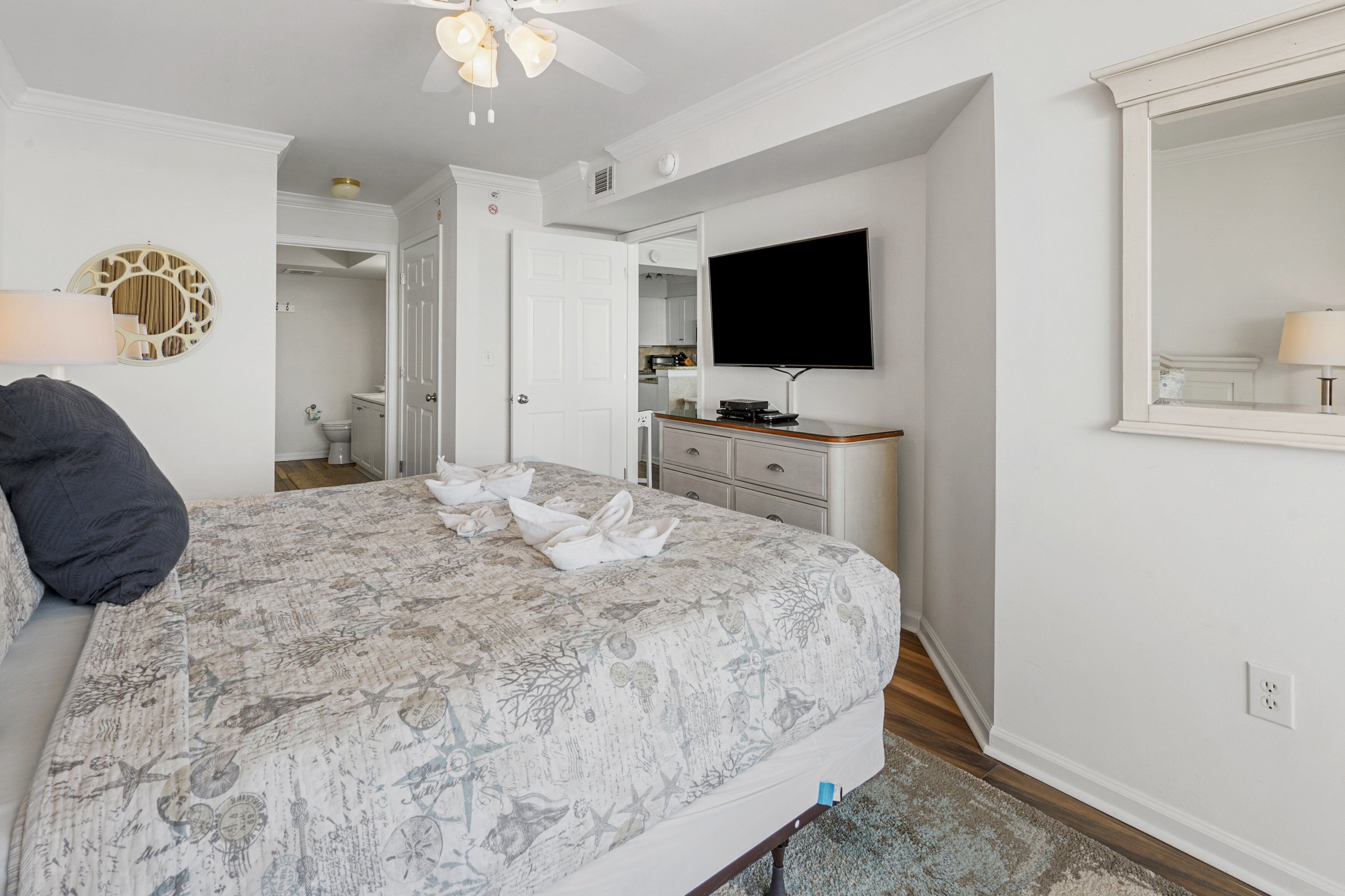 Een slaapkamer met een groot bed, een flatscreen televisie aan de muur, een dressoir en een plafondventilator.
