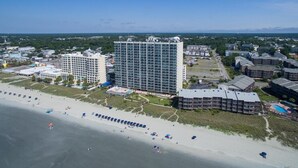 A coastal hotel with multiple buildings, a beach, and a clear sky. - Ashworth 1809 4 Bedroom Condo by RedAwning (North Myrtle Beach)